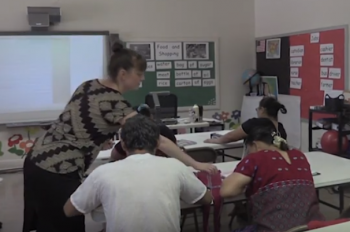 Adult ESL teacher talking to two learners sitting at a table
