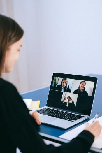 a person is looking at a laptop displaying a virtual meeting with three other participants